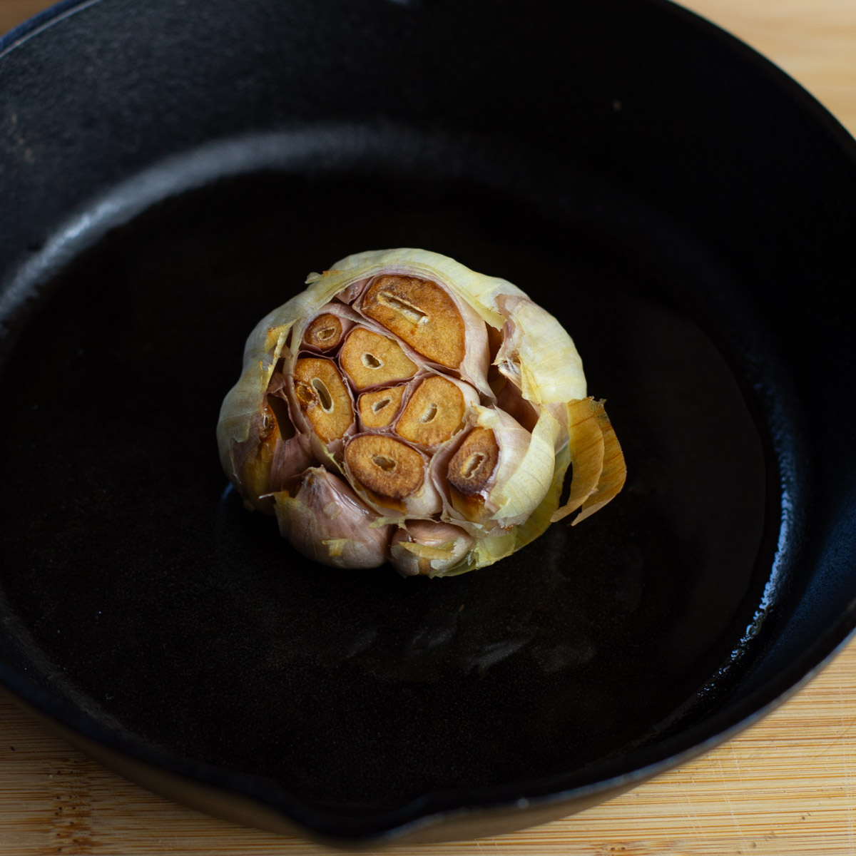 Head of roasted garlic with the top sliced off roasted in a cast iron pan.
