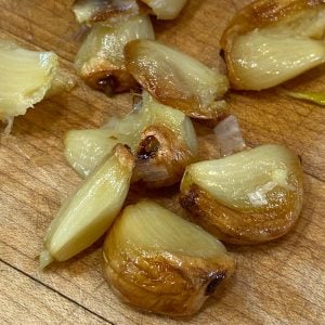 Cloves of roasted garlic on a wood cutting board.