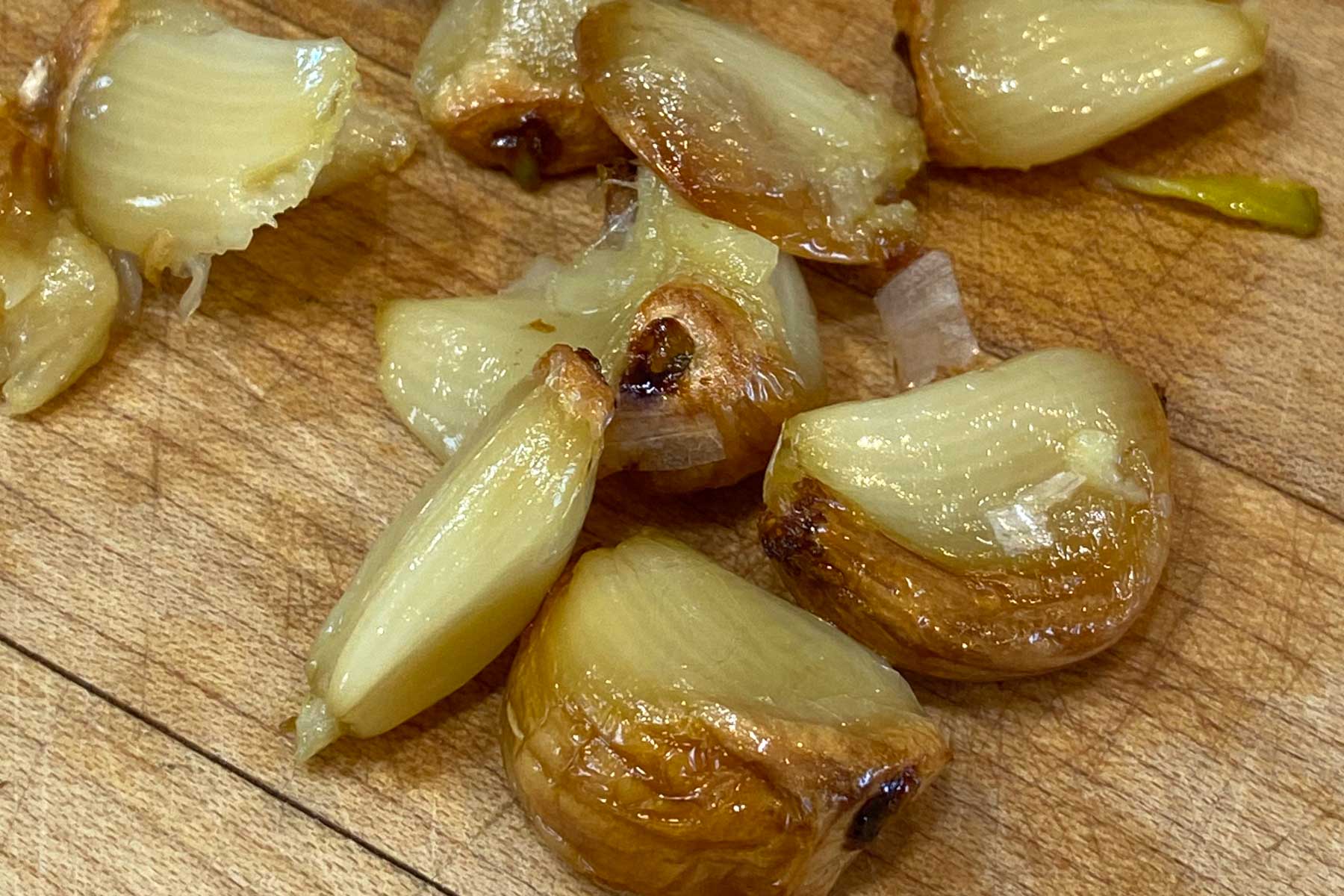 Cloves of roasted garlic on a wood cutting board.