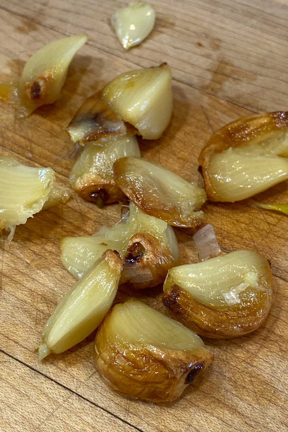 Cloves of roasted garlic on a wood cutting board.