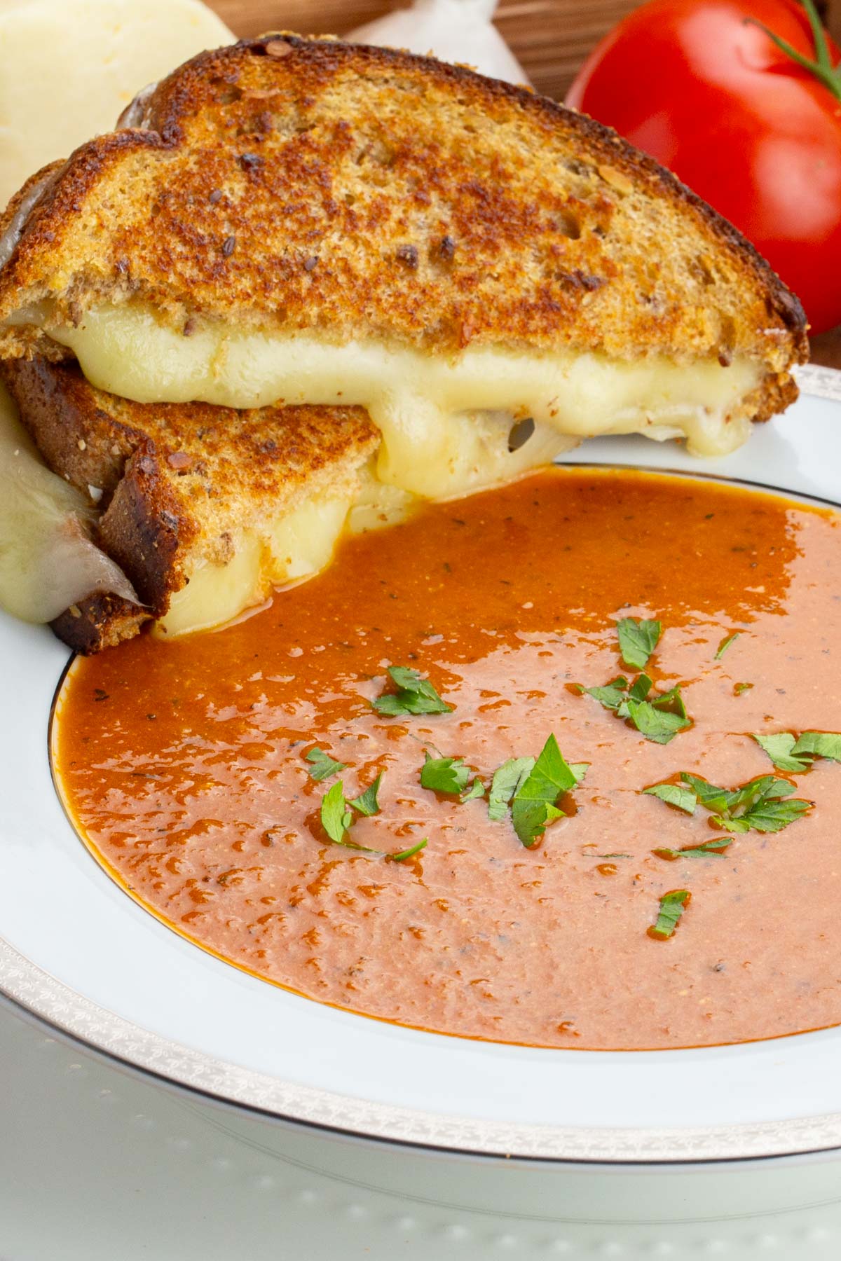 Grilled cheese sandwich with melting cheese on golden bread, paired with a bowl of vibrant tomato soup garnished with fresh parsley.