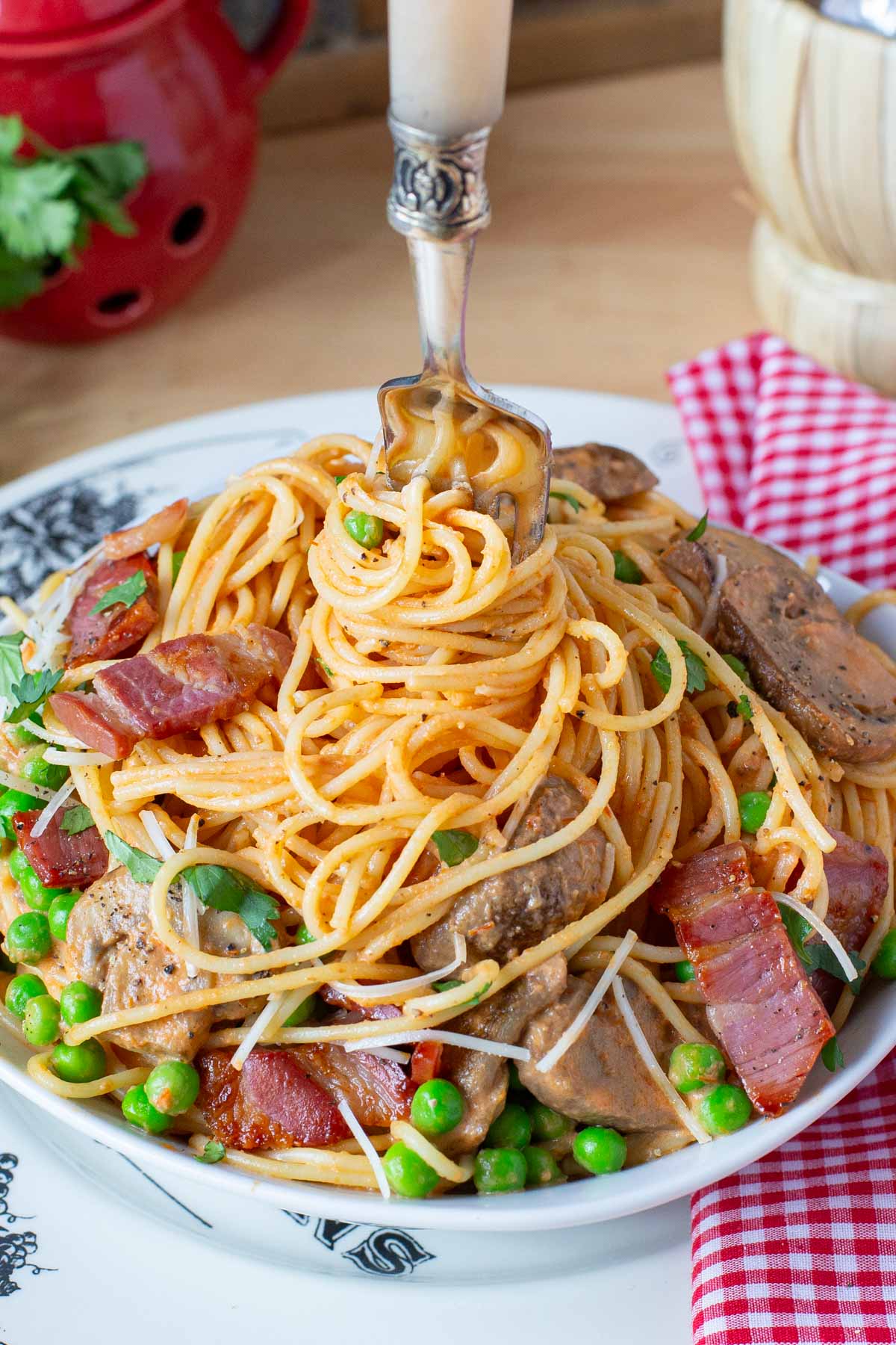 A plate of spaghetti with a fork twirling the pasta, topped with bacon, peas, and mushrooms and garnished with parsley.