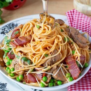 A plate of spaghetti with a fork twirling the pasta, topped with bacon, peas, and mushrooms and garnished with parsley.