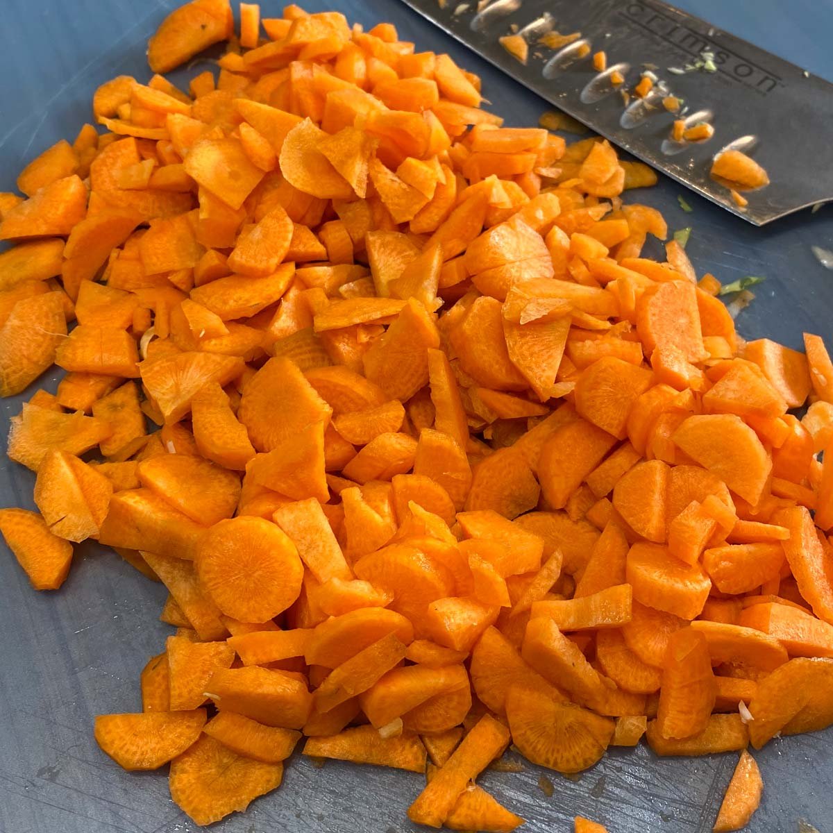 Chopped carrots scattered on a cutting board beside a sharp kitchen knife.