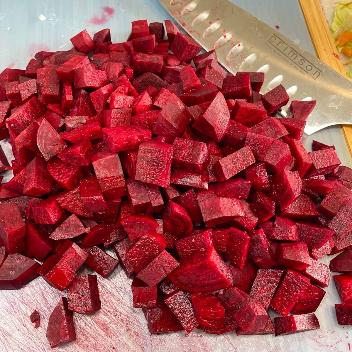 Chopped beets scattered on a cutting board beside a sharp kitchen knife.
