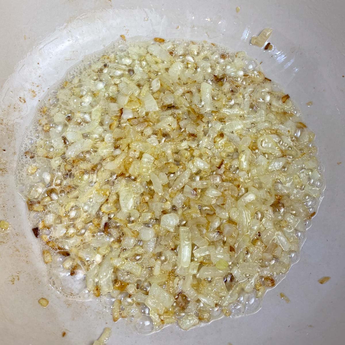 Chopped onions sautéing in oil, turning golden brown, in a pan.