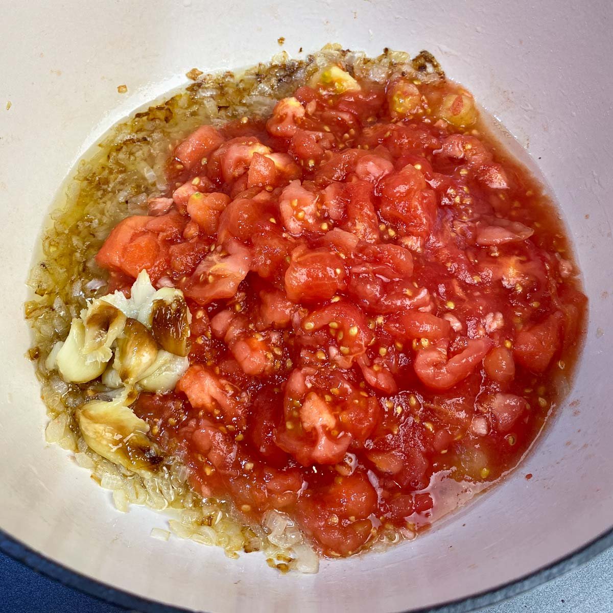 Chopped onions and tomatoes and roasted garlic sautéing in a dutch oven pan.
