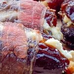 Crisp bacon-wrapped dates stuffed with cheese are placed on a wooden board. Sliced jalapeños along side.