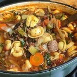 Dutch oven of a hearty soup with tortellini, ground meat, carrots, zucchini, and spinach in a rich, tomato-based broth.
