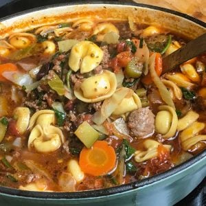 Dutch oven of a hearty soup with tortellini, ground meat, carrots, zucchini, and spinach in a rich, tomato-based broth.