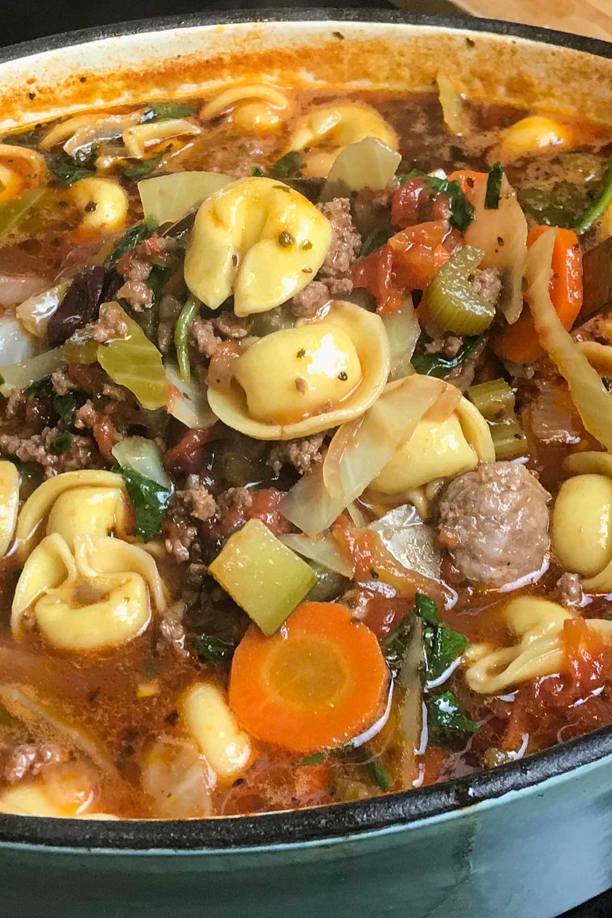 Dutch oven of a hearty soup with tortellini, ground meat, carrots, zucchini, and spinach in a rich, tomato-based broth.