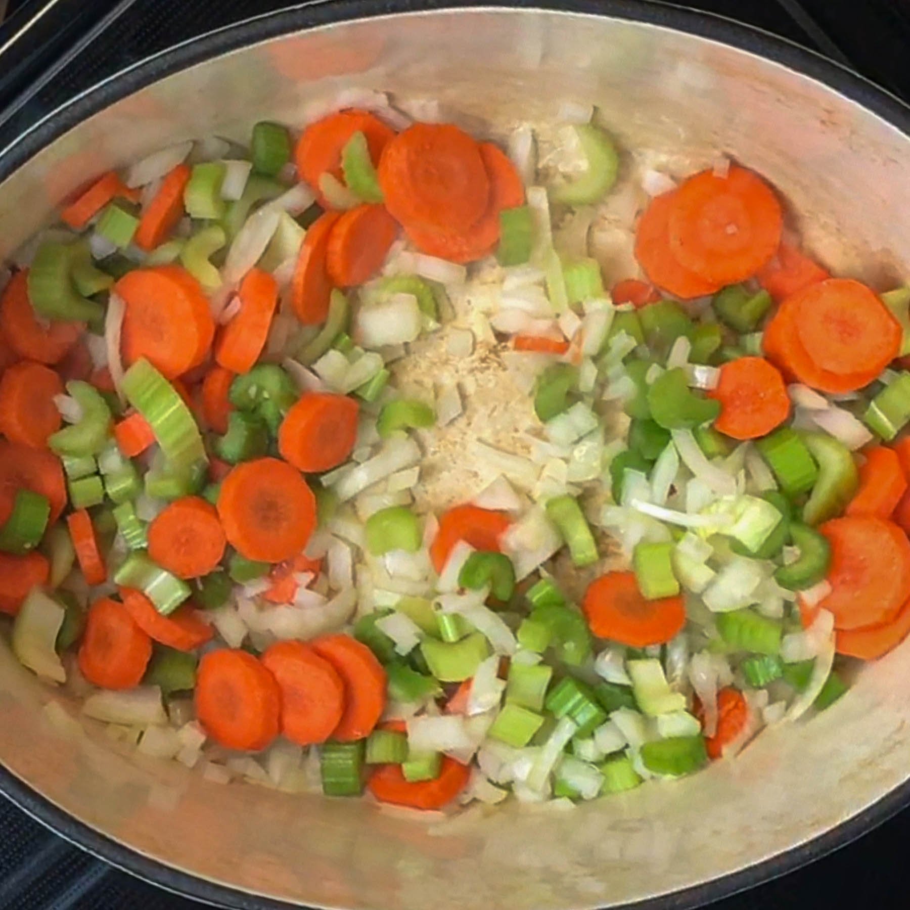 A pot of diced vegetables including carrots, celery, and onions, sautéing on a stovetop.