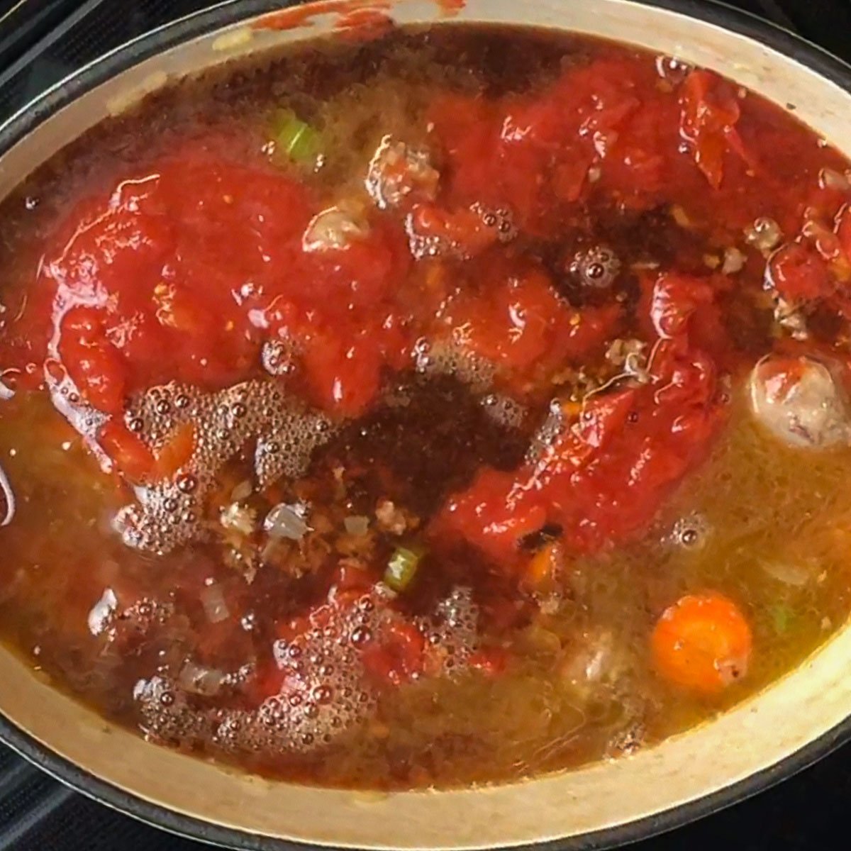 Simmering pot of soup with visible chunks of tomatoes, carrots, and meat.