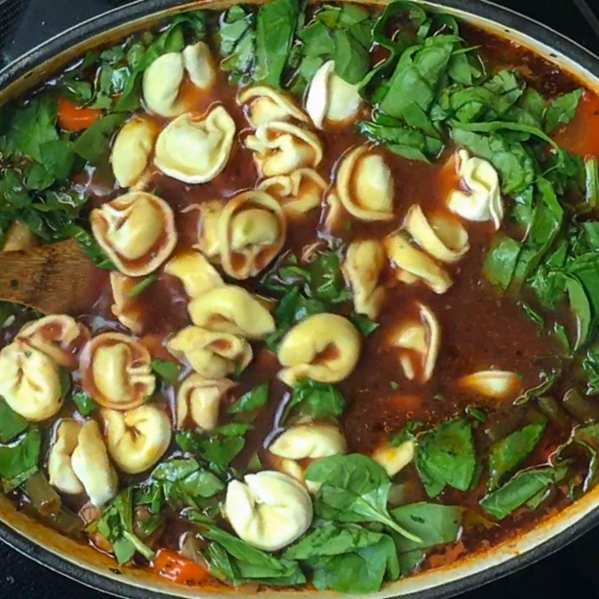 A pot of tortellini soup with vibrant greens, colorful vegetables, and plump tortellini in a rich tomato broth.