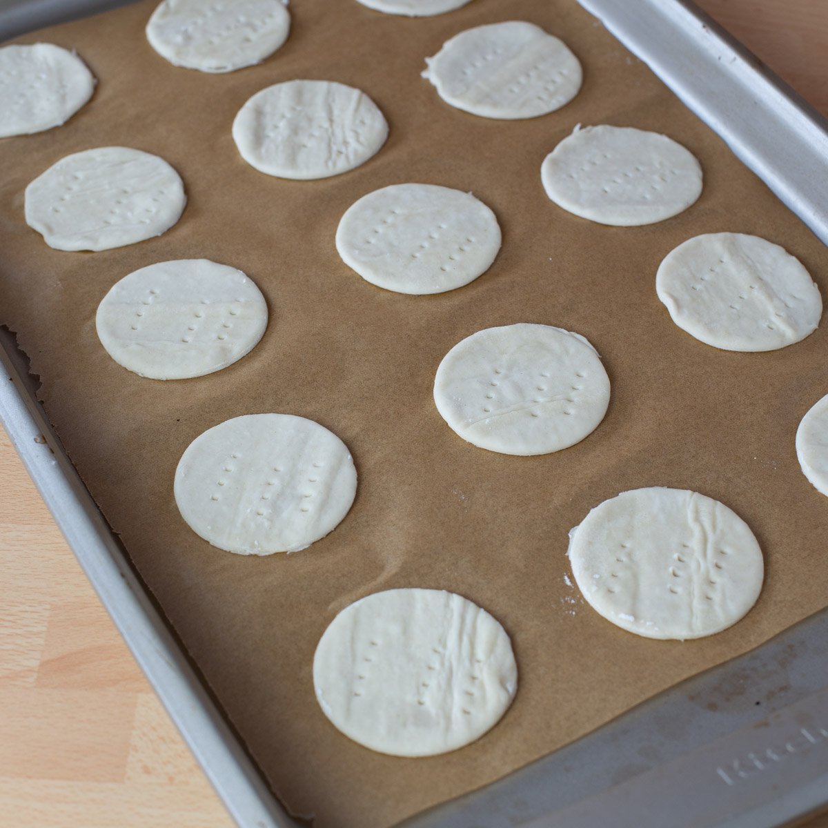 Rows of small, round unbaked pastries on brown parchment paper lined baking sheet.