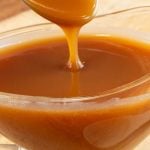 Spoon drizzling caramel sauce into a glass serving dish filled with sauce.