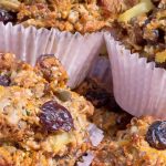Hearty muffins with dried cherries, nuts, and seeds in paper liners fill a red gingham cloth lined basket.