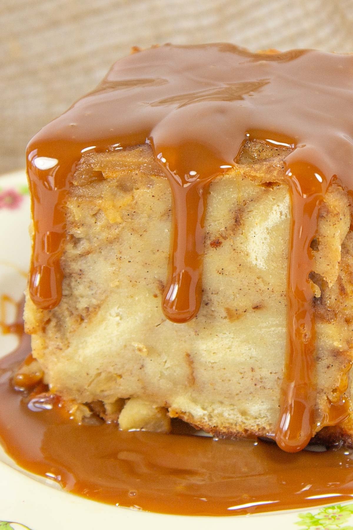 Bread pudding square drenched in glossy caramel sauce sits on a floral plate.