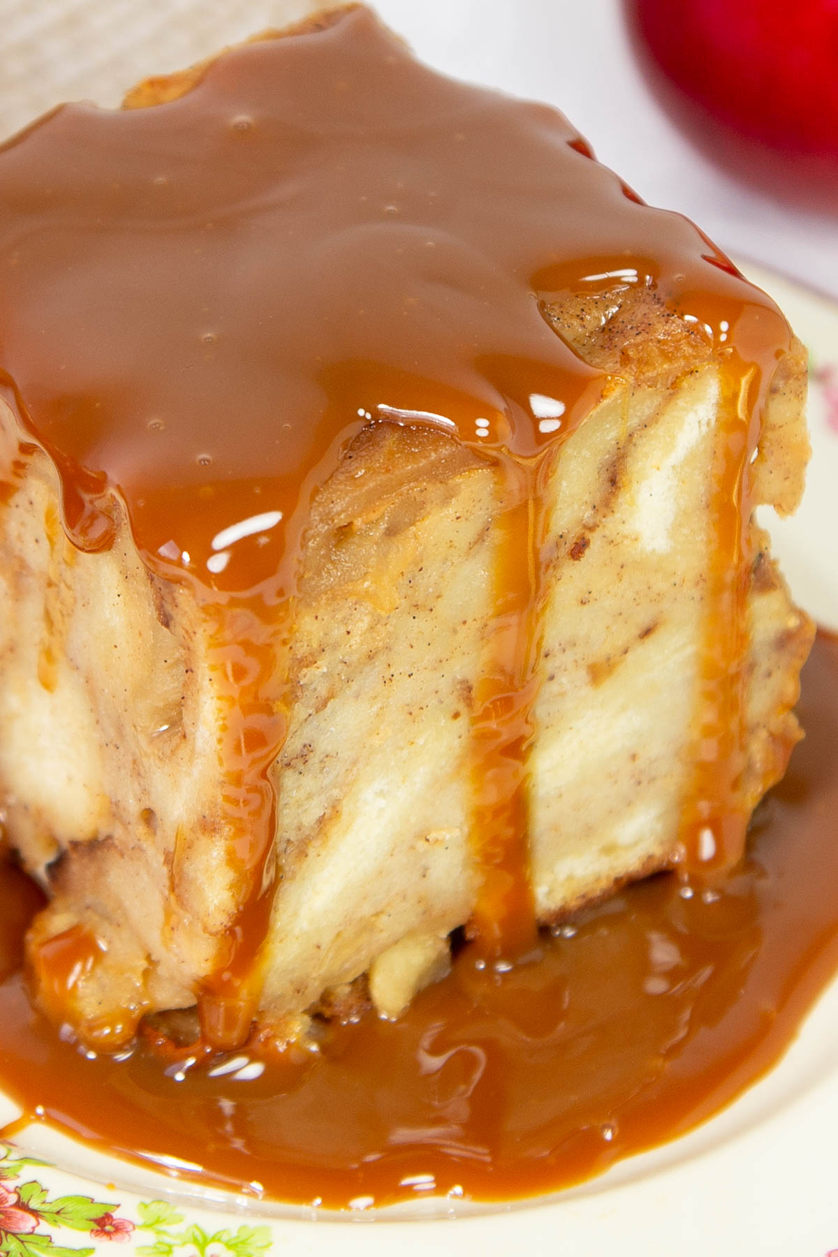 Bread pudding square drenched in glossy caramel sauce sits on a floral plate.