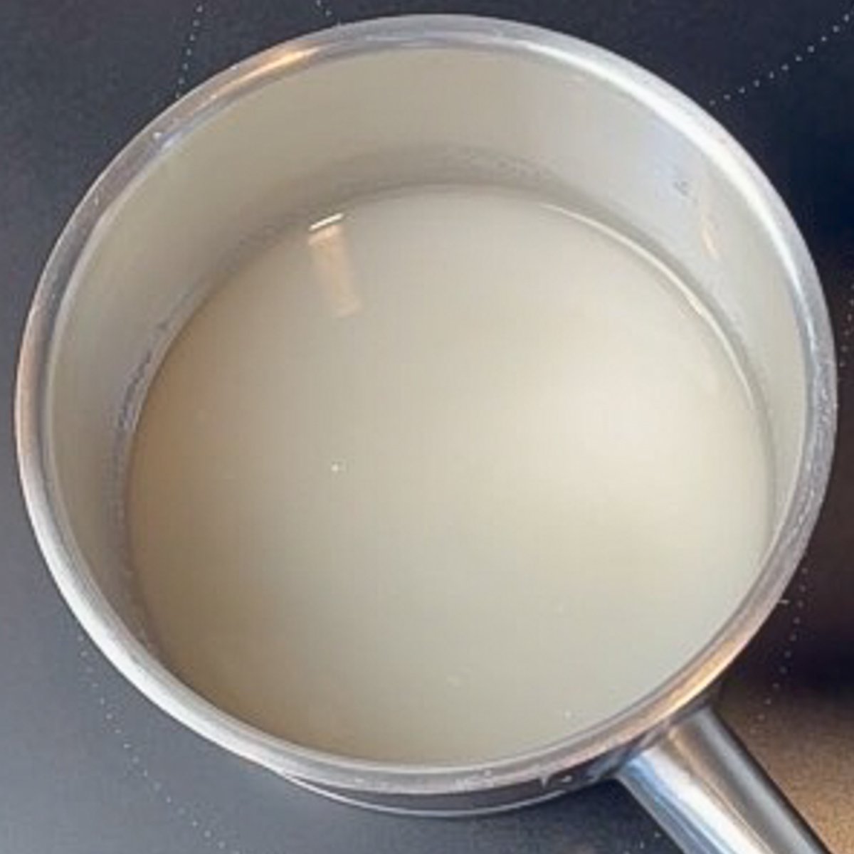 A metal saucepan filled with water and sugar sits on a black stovetop.