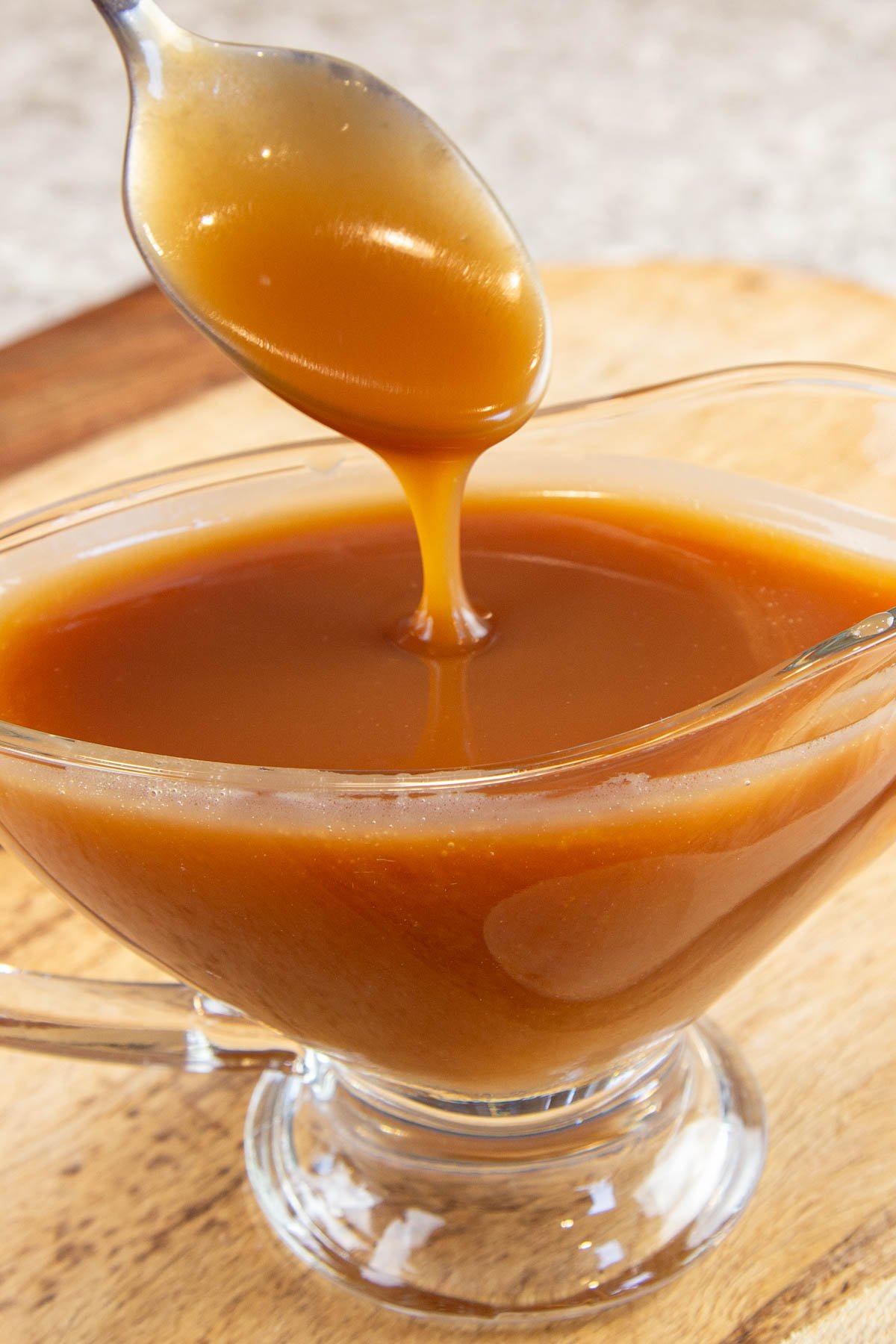 Spoon drizzling caramel sauce into a glass serving dish filled with sauce.