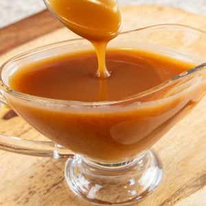 Spoon drizzling caramel sauce into a glass serving dish filled with sauce.