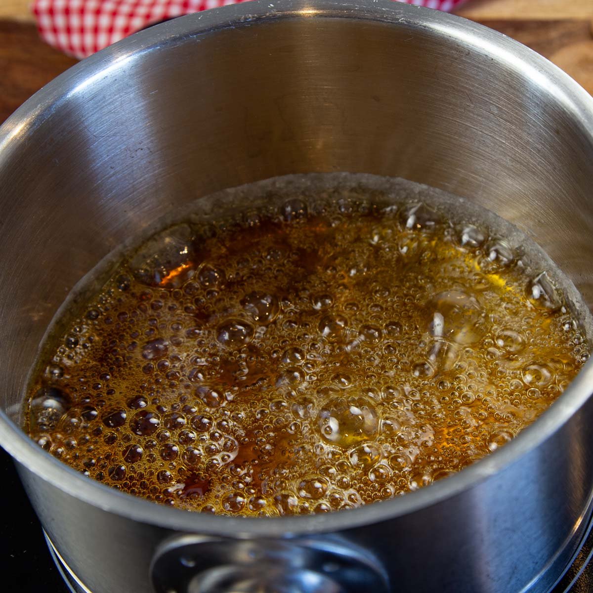 A stainless steel pot with bubbling, dark-colored caramel sauce on a stove.