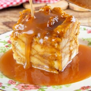 A square piece of bread pudding is drenched in rich caramel sauce on a floral plate.