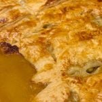 Close-up of chicken pot pie with puff pastry, showcasing a flaky crust with gravy oozing out. Text reads "Chicken Pot Pie with Puff Pastry."