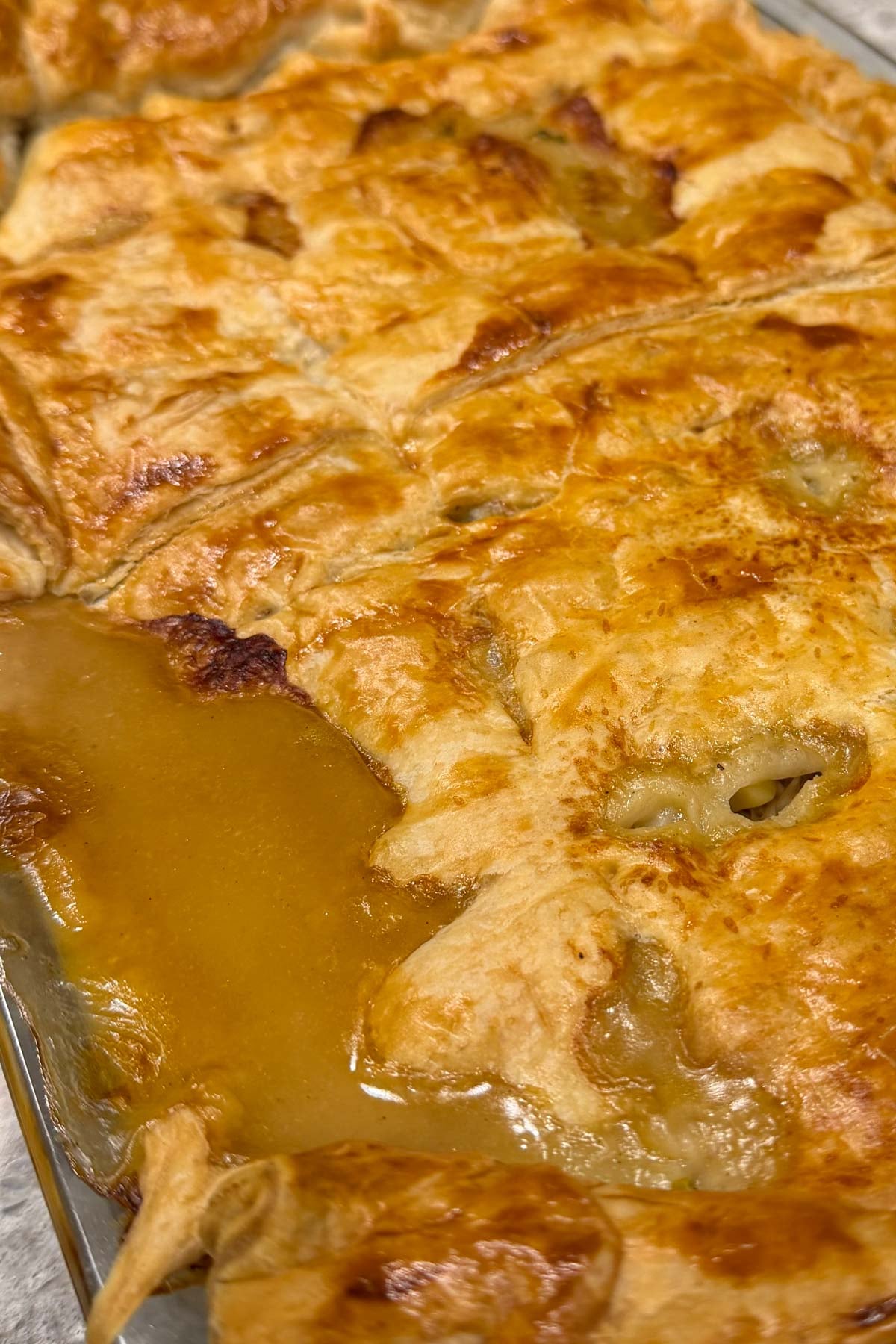 Golden brown pastry covers a homemade chicken pie in a rectangular dish, with gravy oozing out.
