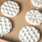Five unbaked shortbread cookies with intricate patterns rest on a parchment-lined baking sheet.