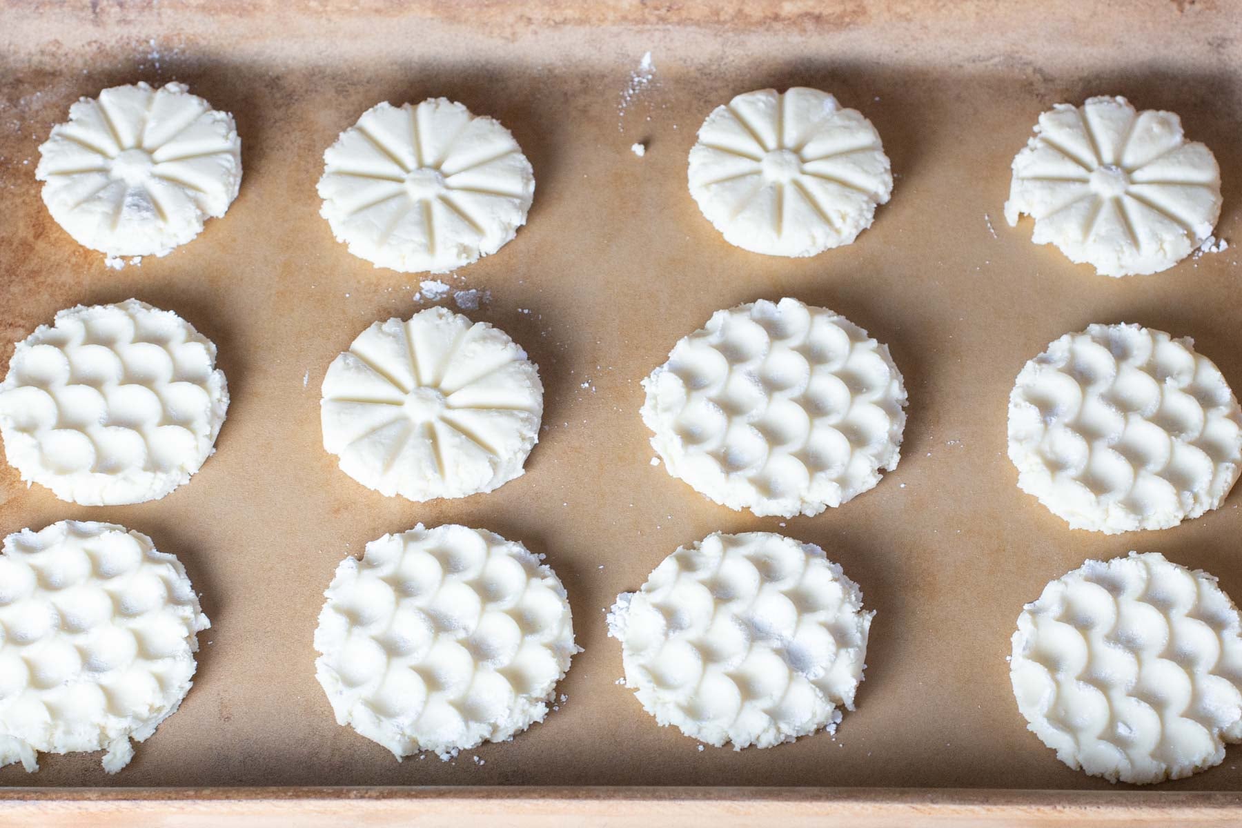 Twelve unbaked shortbread cookies with intricate patterns rest on a parchment-lined baking sheet.