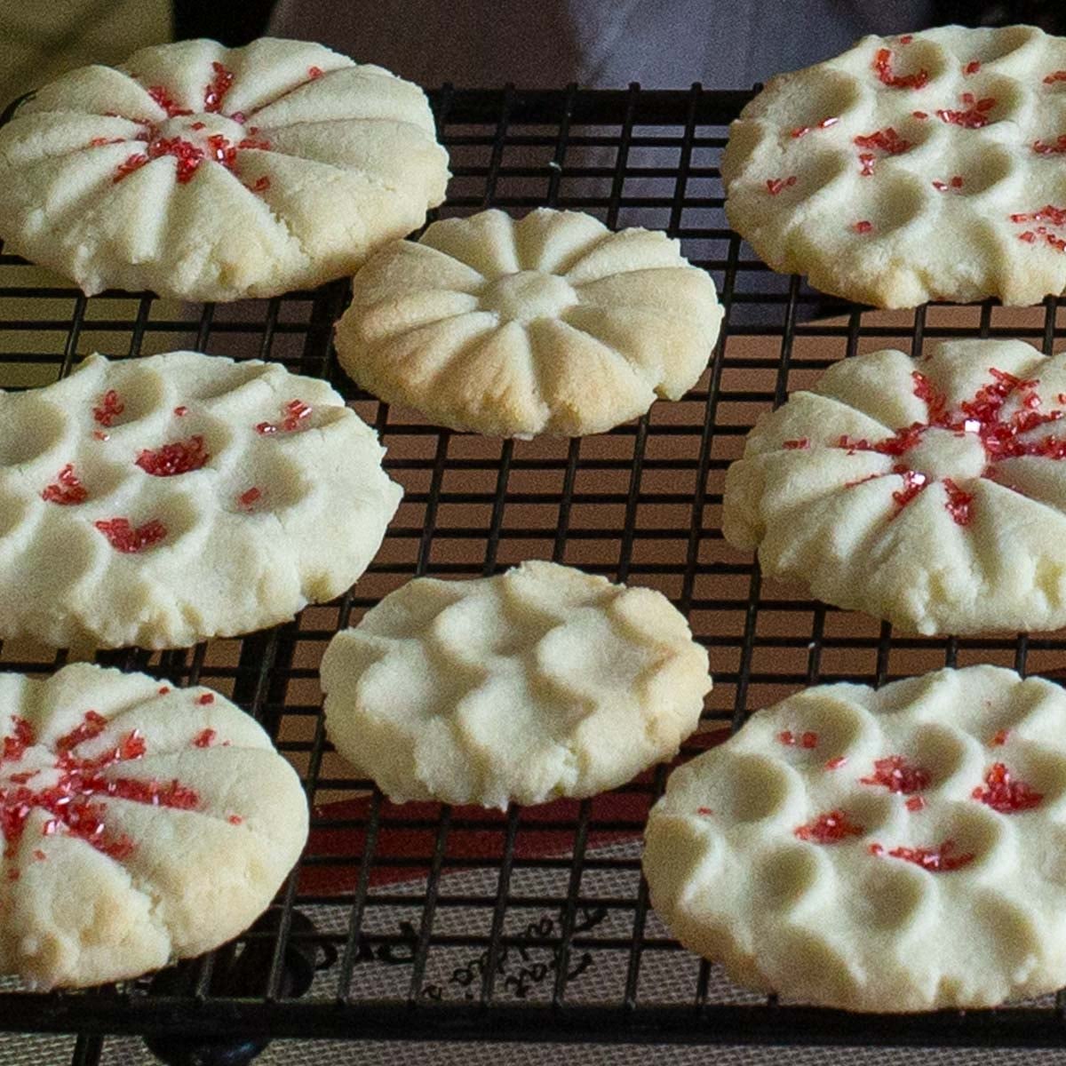 Assorted homemade cookies with scalloped edges and red sprinkles cooling on a black wire rack.
