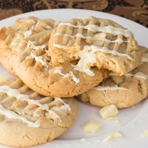 A plate of white chocolate pudding cookies drizzled with white chocolate. One cookie has a bite taken, revealing a soft texture.