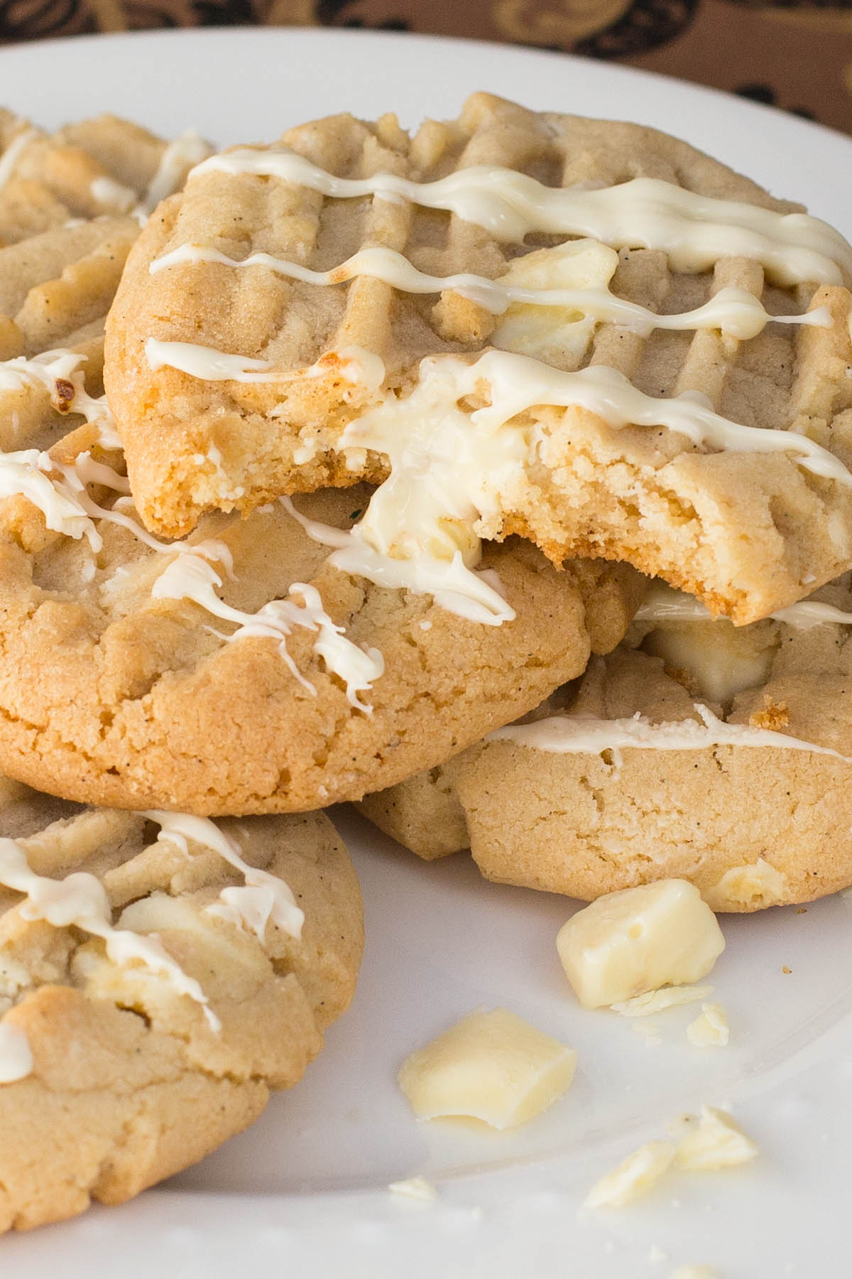 A plate of white chocolate pudding cookies drizzled with white chocolate. One cookie has a bite taken, revealing a soft texture.