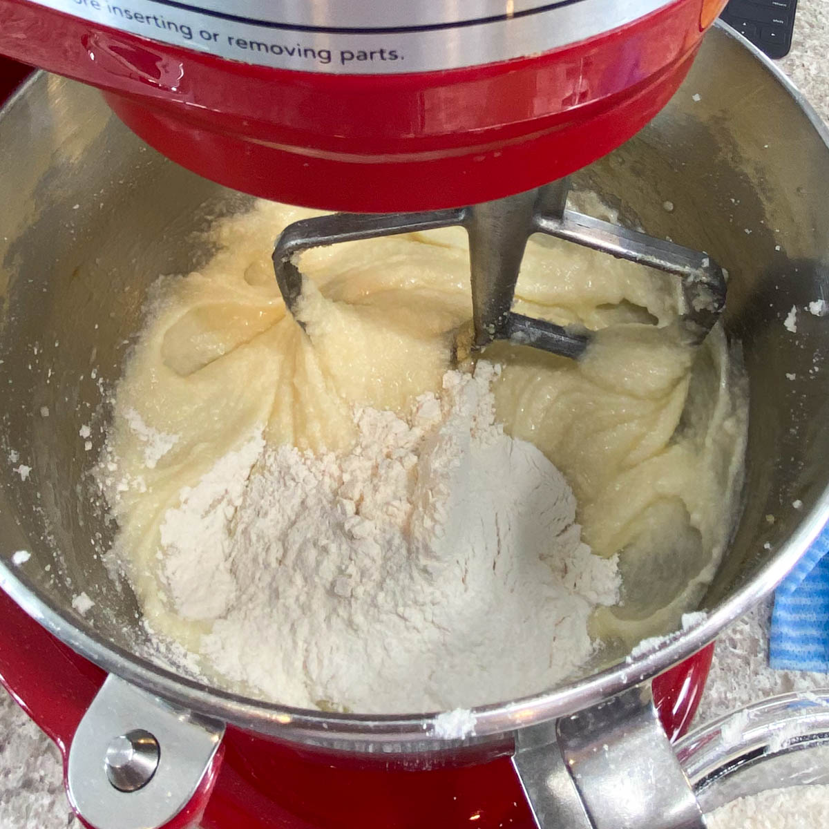 Close-up of flour being added to a creamy batter in a red stand mixer.