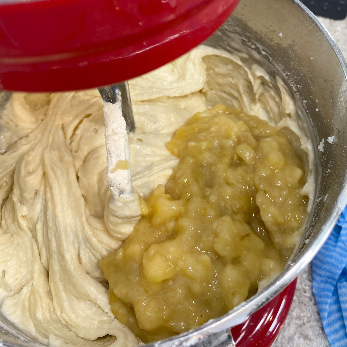 Close-up of mashed bananas being added to a creamy batter in a red stand mixer.