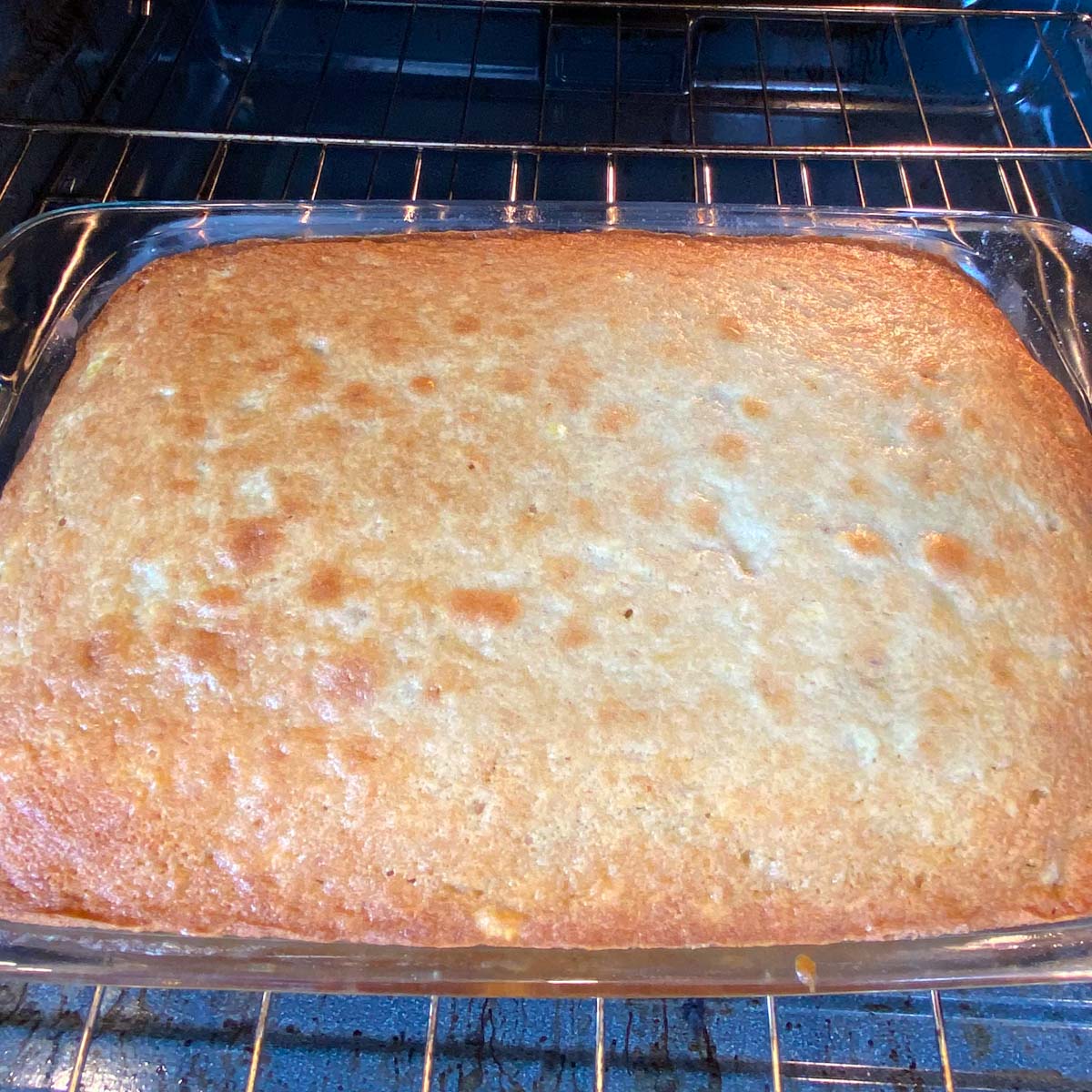 Golden, freshly-baked cake in a glass dish inside an oven.