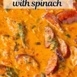 Creamy sauce in a stainless steel skillet with sliced sausage, spinach, and tomatoes.
