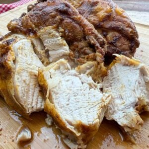 Roasted chicken breasts, golden-brown and juicy, sliced and displayed on a wooden board.