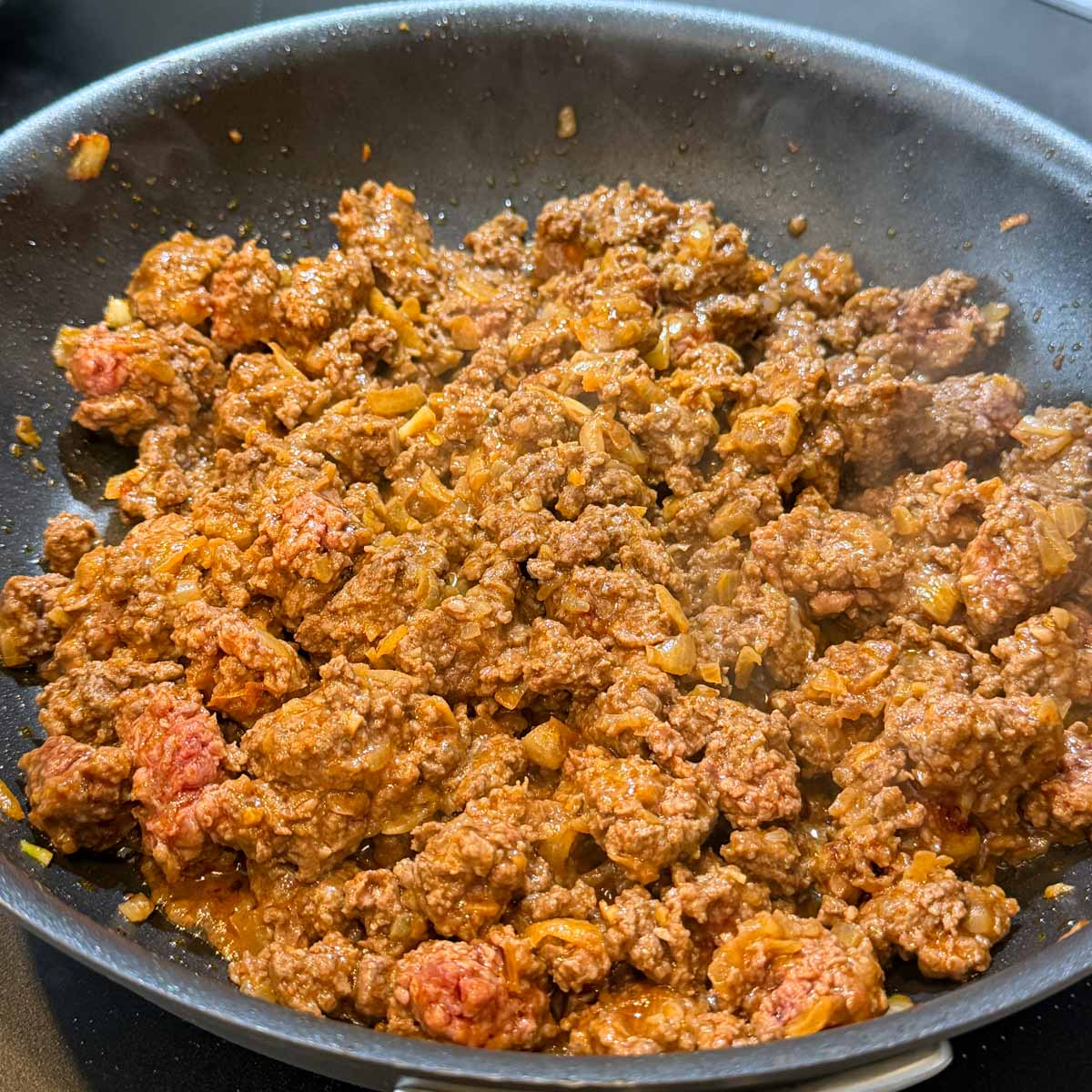 Ground beef is sizzling in a pan, mixed with diced onions and spices.