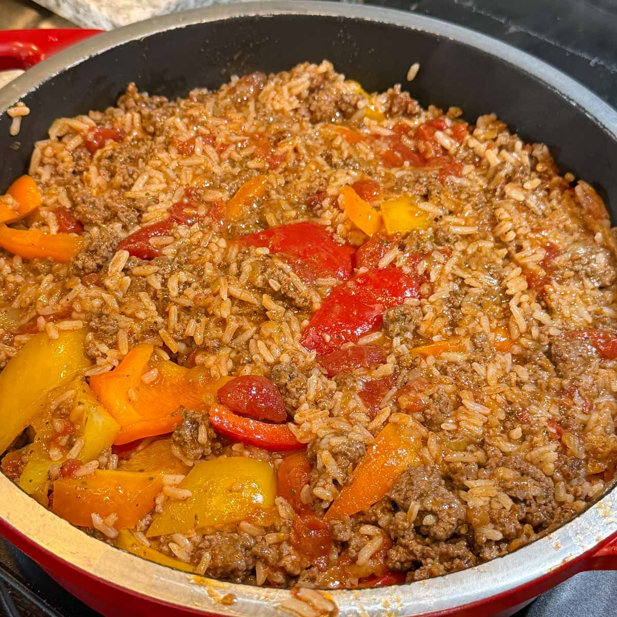 A skillet dish casserole with cooked rice, ground beef, and vibrant red, yellow, and orange bell peppers.