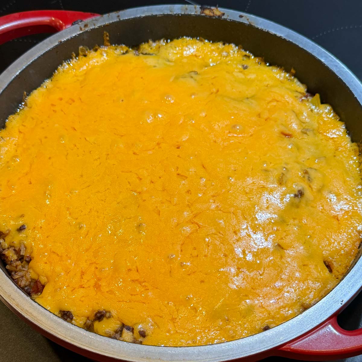 A round, red-handled baking dish filled with a bubbling, cheddar cheese-topped casserole.