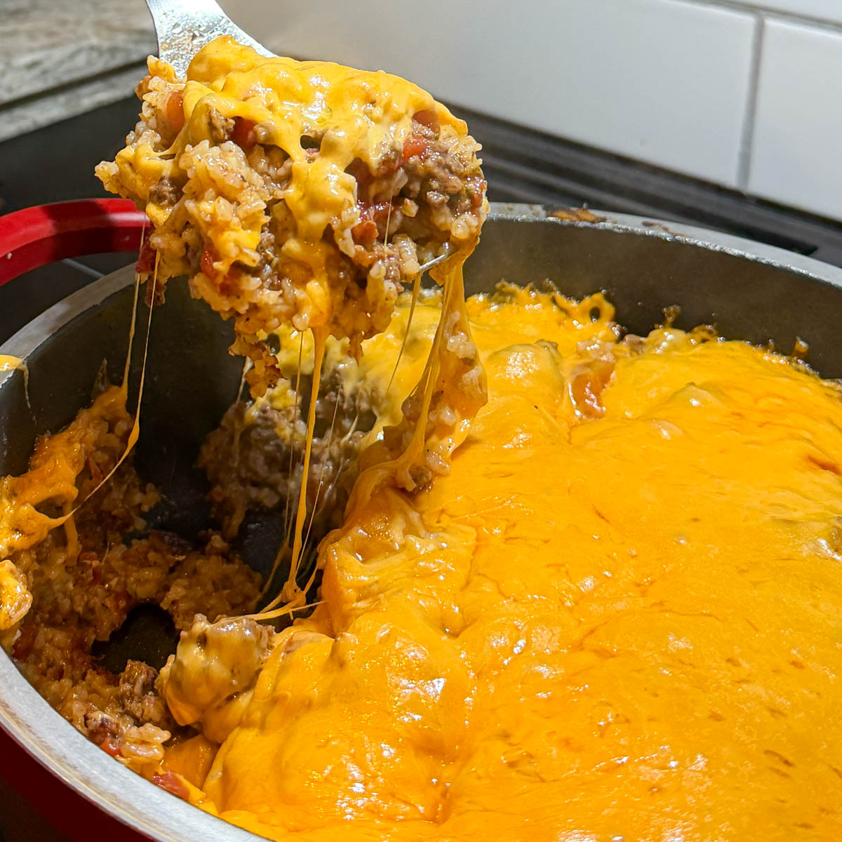A spoonful of cheesy beef and rice casserole is lifted from a large pan, showcasing melted cheddar cheese.
