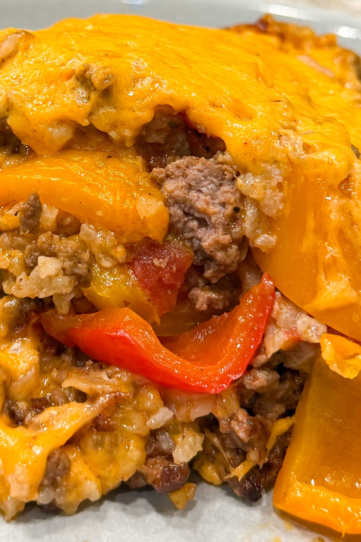 Cheesy casserole dish featuring layers of melted cheddar, browned ground beef, red and yellow bell peppers, and rice on a blue plate.