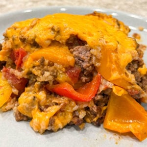 Cheesy casserole dish featuring layers of melted cheddar, browned ground beef, red and yellow bell peppers, and rice on a blue plate.