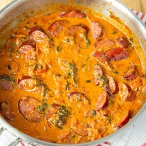 Creamy sauce in a stainless steel skillet with sliced sausage, spinach, and tomatoes.