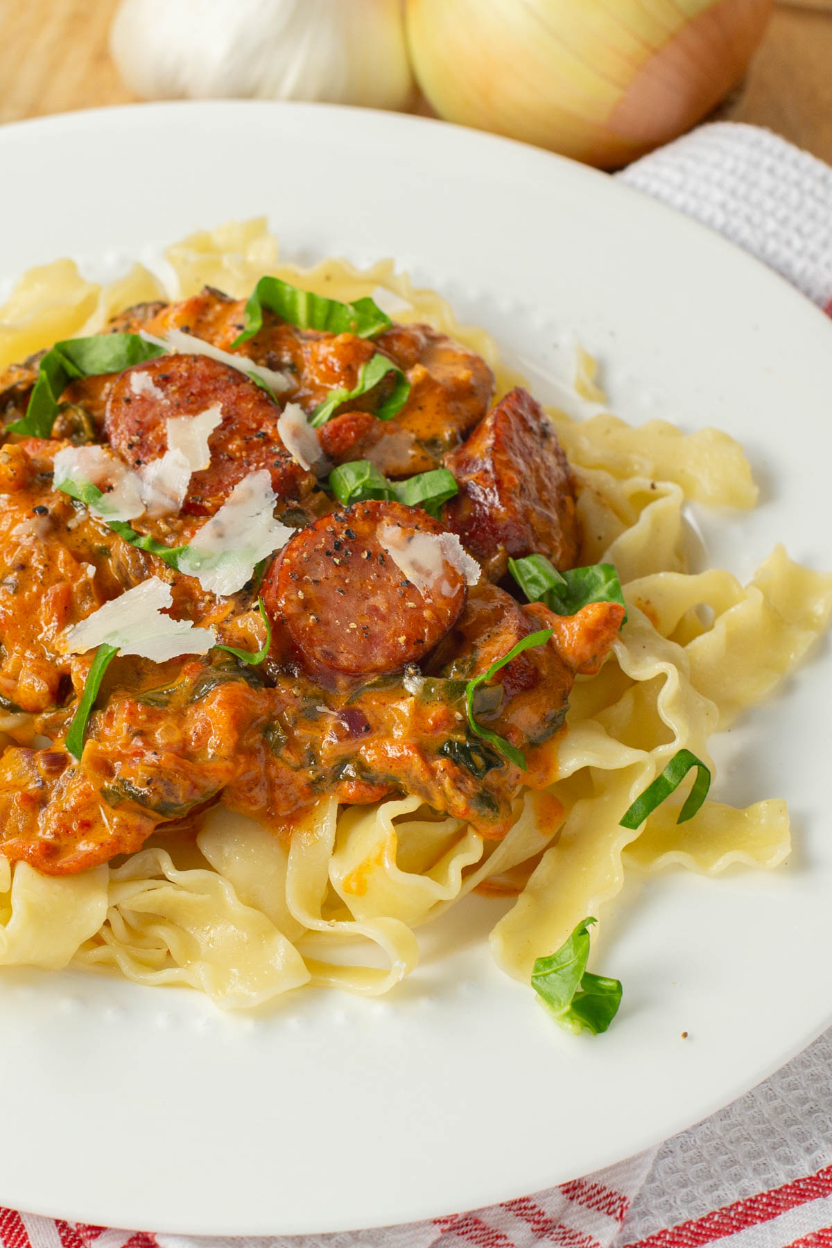 A plate of ribbon pasta topped with a rich, creamy tomato sauce, slices of sausage, garnished with fresh spinach, and shaved parmesan.