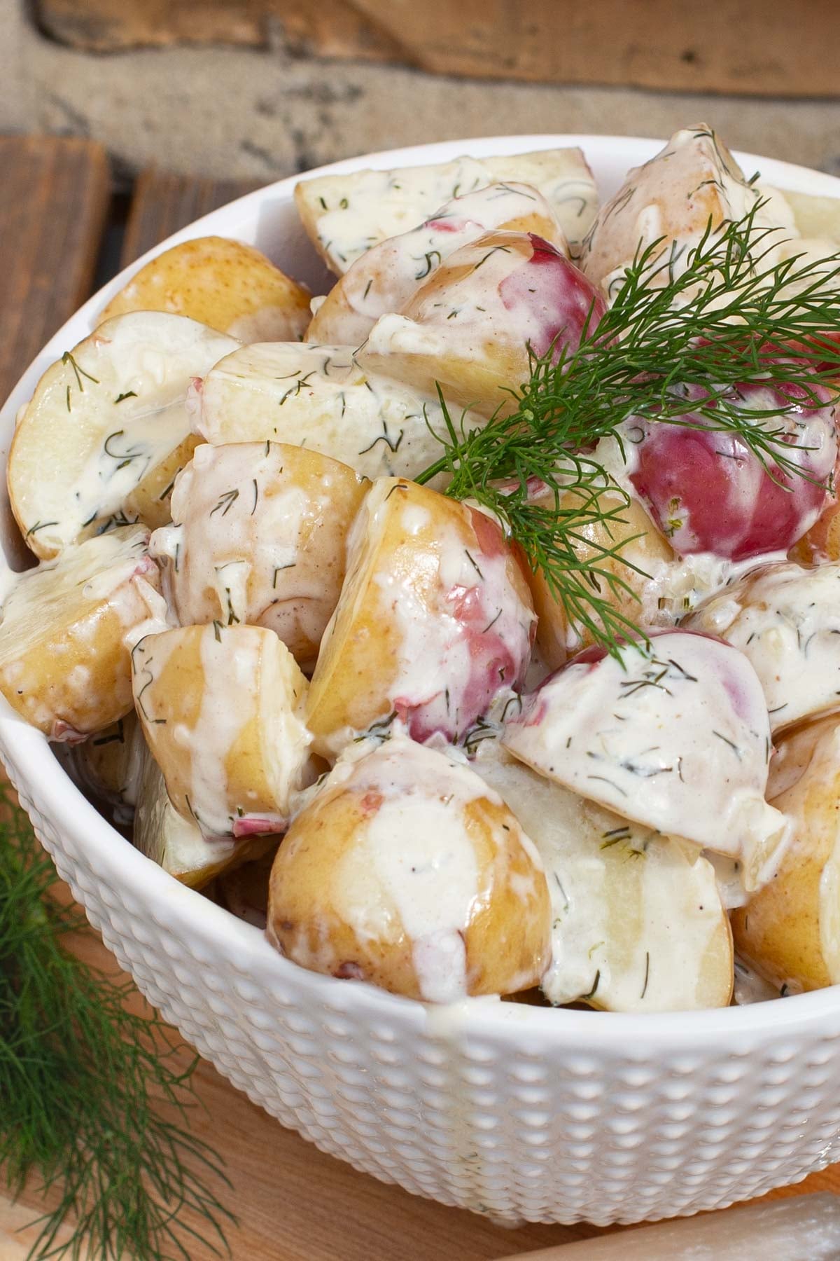 A white bowl of new potatoes coated in a creamy dill sauce garnish with a fresh sprig of dill.garnished with fresh dill.