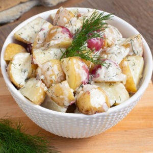 A white bowl of new potatoes coated in a creamy dill sauce garnish with a fresh sprig of dill.